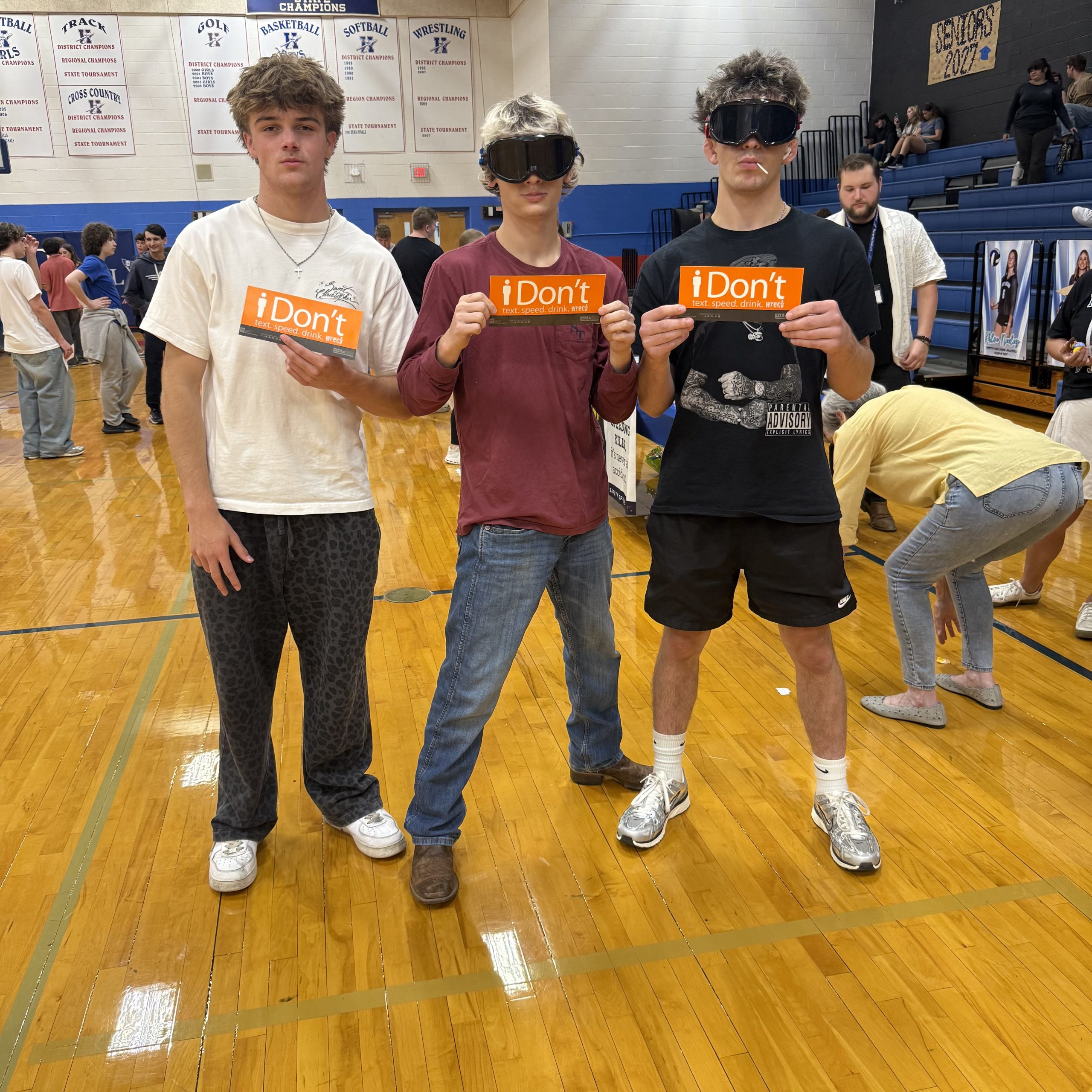 Students wearing Fatal Vision goggles hold iDont signs in a gym